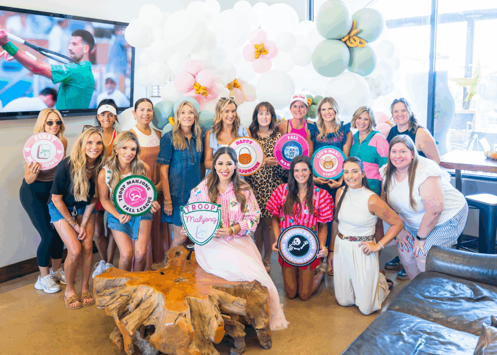 Group photo of stylishly dressed women holding Troop Mahjong merit badges and the Troop Mahjong crest logo.